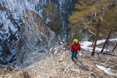 man with backpack stand on slope of rock with trees on foot, Russia, Lake Baikal clipart
