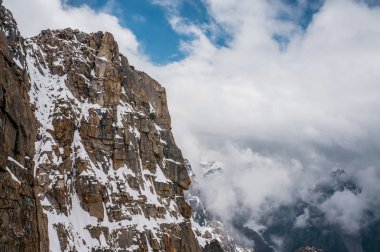 view of rocky slope with snow against clouds in sky, Ala Archa National Park, Kyrgyzstan clipart
