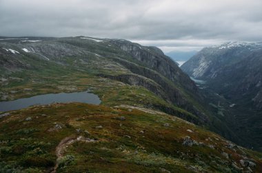 view of hill slope with grass and small pond, mountains on background, Norway, Hardangervidda National Park