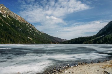view of lake with ice on surface and mountains on background, Morskie Oko, Sea Eye, Tatra National Park, Poland clipart