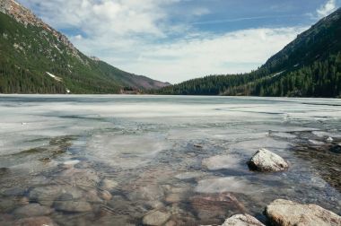 view of stones on water surface on shore with hills on background, Morskie Oko, Sea Eye, Tatra National Park, Poland clipart