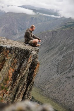 Cliff üzerinde oturan ve güzel manzara, Altay, Rusya arayan genç adam