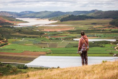 back view of man looking at beautiful landscape with agricultural fields and mountains, vietnam, dalat region clipart