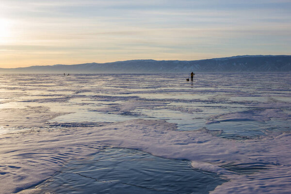 male hiker with backpack walking on ice water surface against hills on shore,russia, lake baikal   