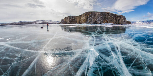 male hiker with backpack standing on ice water surface against rock formation on shore ,russia, lake baikal 