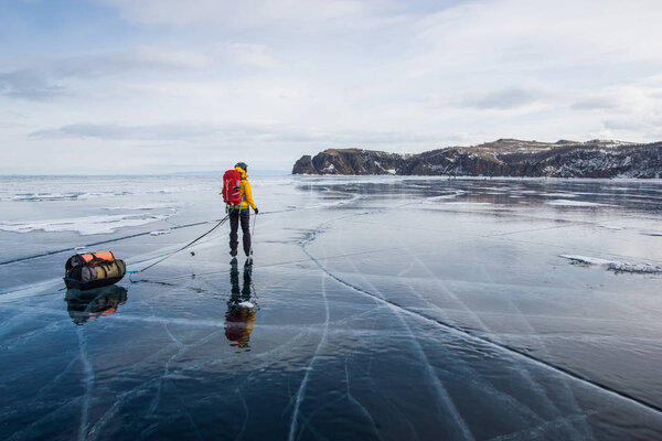 man with backpack going through ice water surface and hills on background, Russia, Lake Baikal