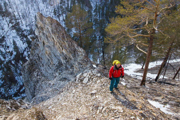 man with backpack stand on slope of rock with trees on foot, Russia, Lake Baikal
