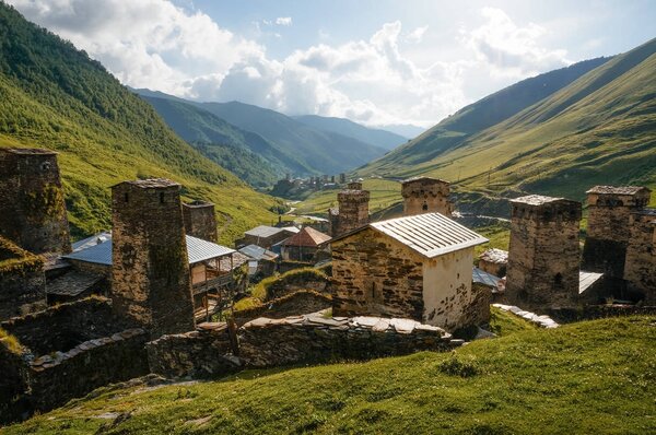 view of grassy field with old weathered rural buildings and hills on background, Ushguli, svaneti, georgia 