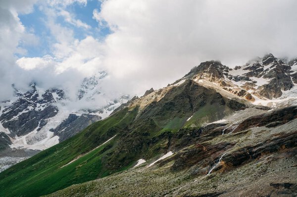 view of snowy mountain peaks with grass on slopes under clouds, Ushguli, svaneti, georgia 