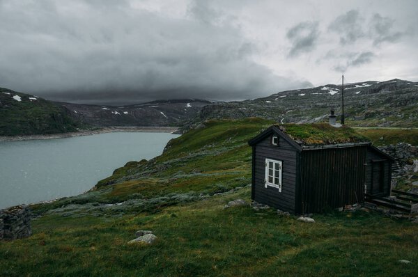 rural house over field with green grass against small pond, Norway, Hardangervidda National Park