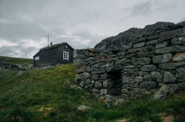 ruined old stone wall and rural house on background over field with green grass, Norway, Hardangervidda National Park