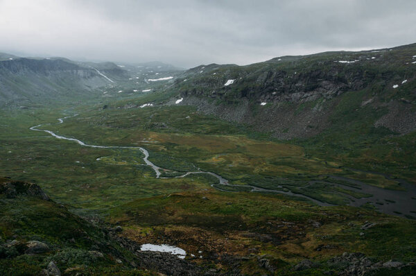 вид на зеленое травяное поле с речным ручьем в окружении скалистых скал, Норвегия, Национальный парк Хардангервидда

