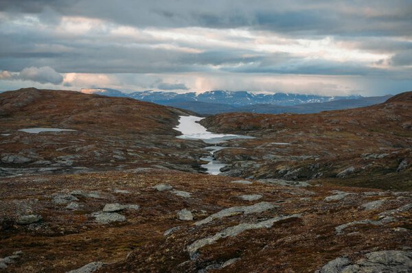 поле с небольшими водоемами и горами на заднем плане во время штормовой погоды, Норвегия, Национальный парк Хардангервидда
