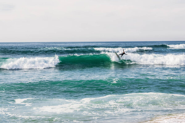 unidentified surfer on surfboard riding wave and beautiful seascape at cloudy day, Portugal 