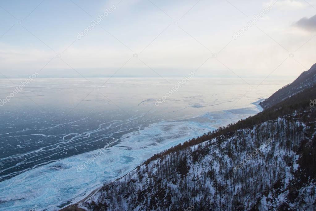 hill slope with trees against ice water surface,russia, lake baikal 