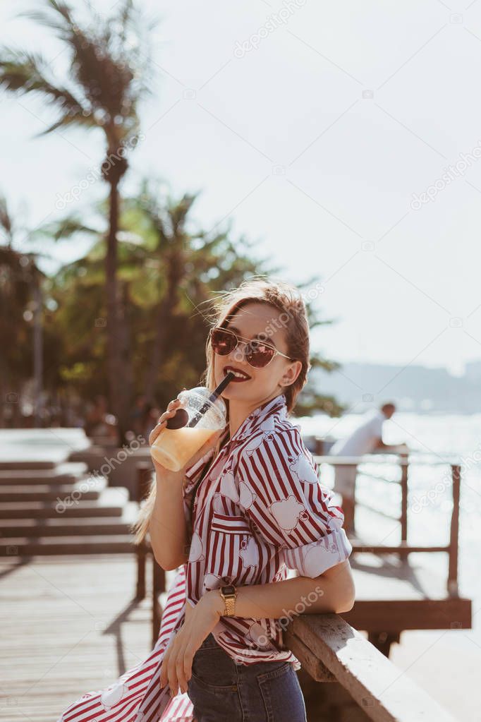 smiling young woman drinking cocktail on pier