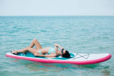young slim girl lying on paddle board on sea at tropical resort clipart