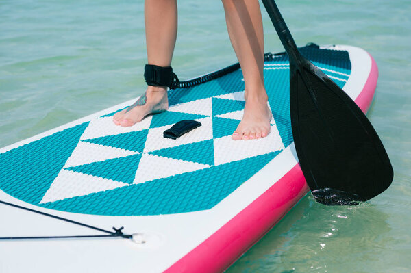 low section view of woman on stand up paddle board on sea at tropical resort