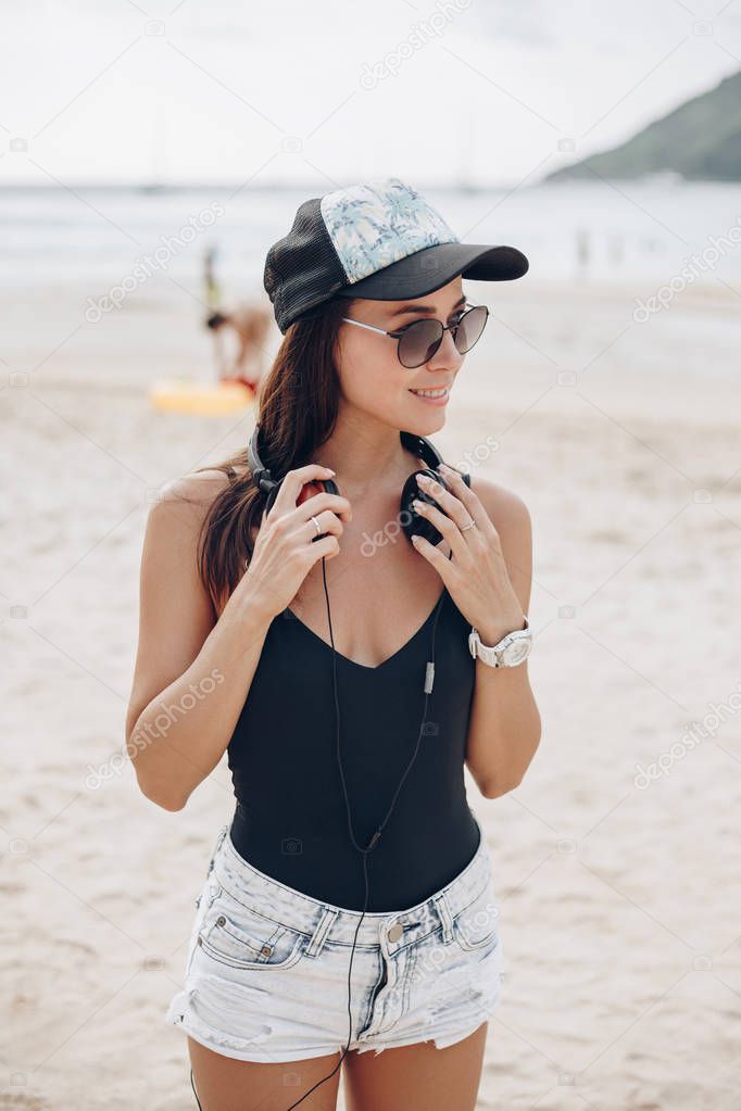 young woman in cap and sunglasses listening music with headphones at beach