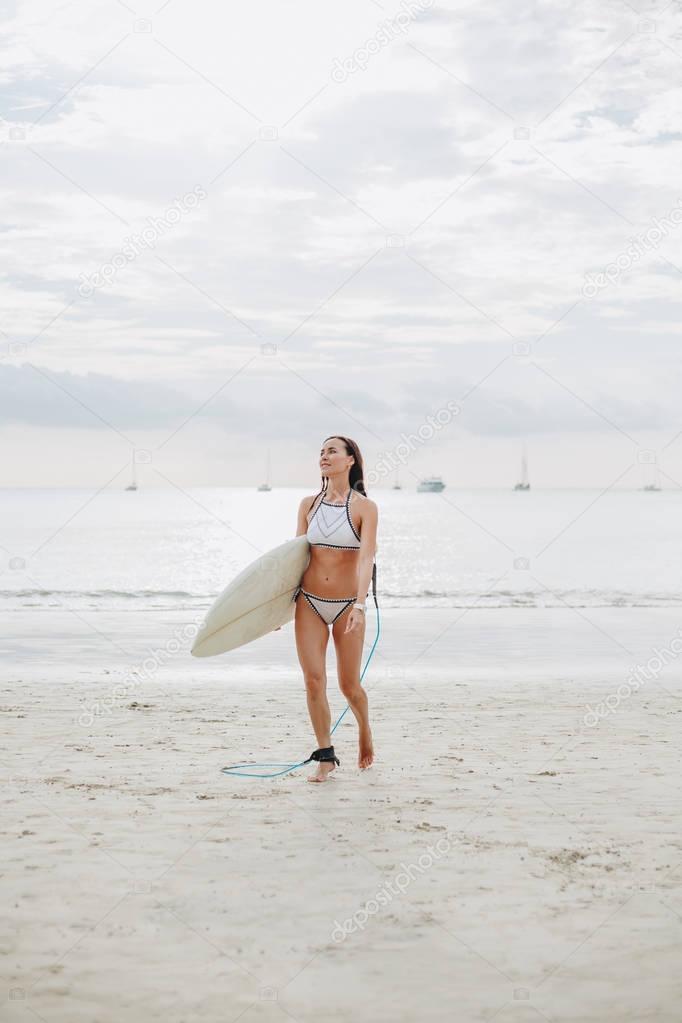 surfer in swimsuit walking with surfboard on beach at sea