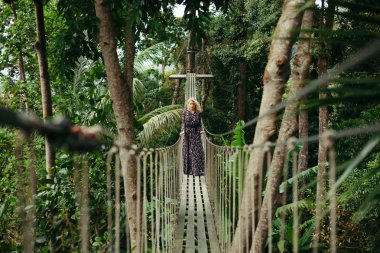 attractive serious woman in dress standing on footbridge in jungle clipart