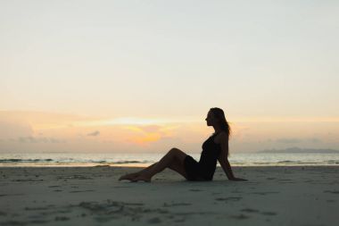 okyanus kumlu sahilde günbatımı sırasında oturan kadın silüeti