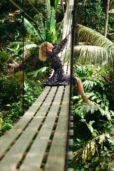 side view of attractive woman posing on suspension bridge in jungle