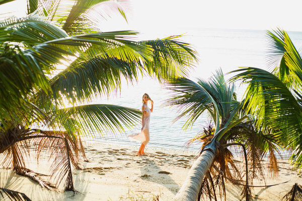 beautiful woman posing between palm trees on ocean beach