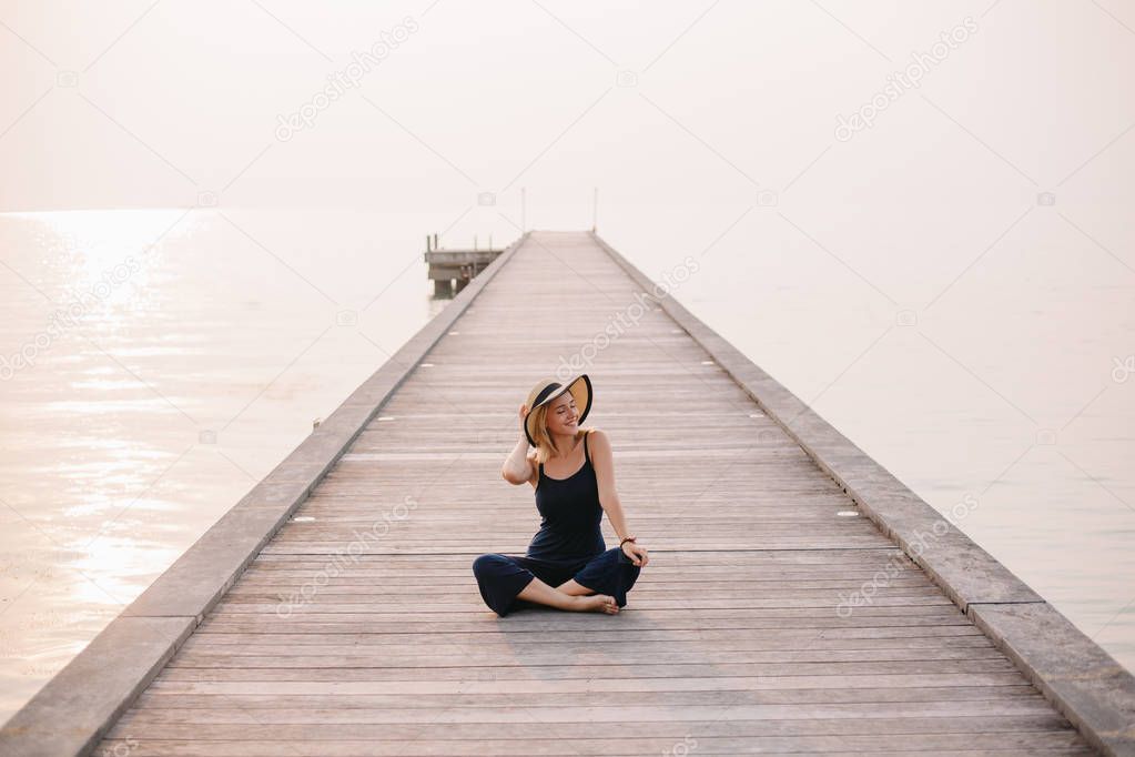 happy beautiful woman in hat sitting on pier near ocean