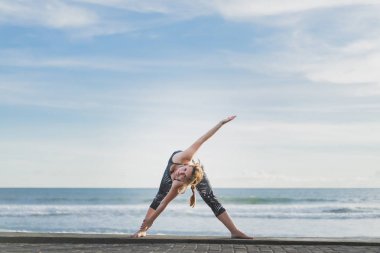 kadın genişletilmiş üçgen Yoga poz okyanus ve mavi gökyüzü arka plan, Bali, Endonezya