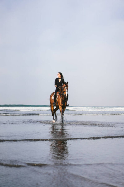 Вид спереди на молодую женщину верхом на лошади с океаном позади
