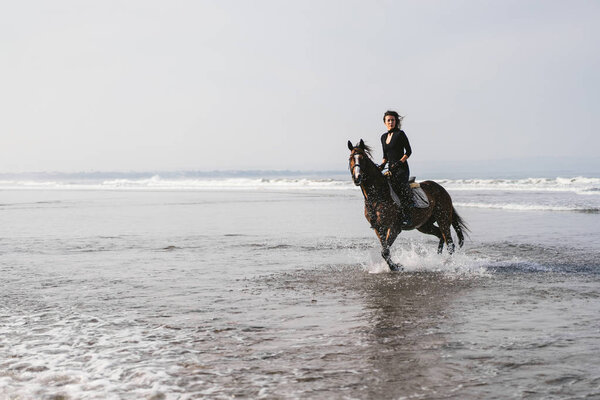 young female equestrian riding horse in water 