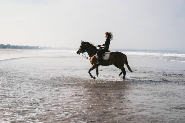 young female equestrian riding horse in water 