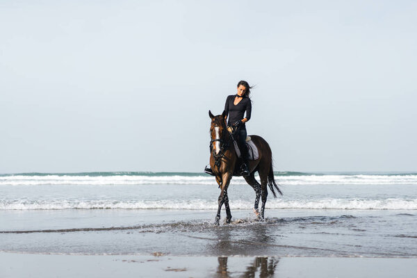front view of female equestrian riding horse in wavy water