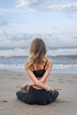 Dikiz pratik yoga lotus poz kolları olan genç kadının arkasından sahil üzerinde geçti.