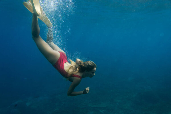 underwater photo of young woman in swimming suit and fins diving in ocean alone