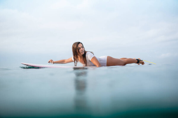 beautiful young woman swimming on surfboard in ocean