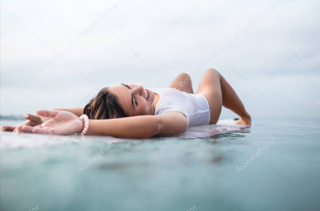 seductive young woman relaxing on surfboard in ocean during summer vacation