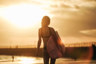 arkadan görünüşü kadın sörfçü günbatımında sörf ile poz