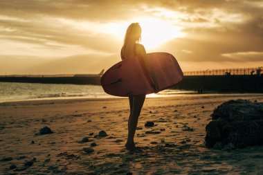 kadın sörfçü arka ışık ile gün batımında sahilde surfboard ile poz