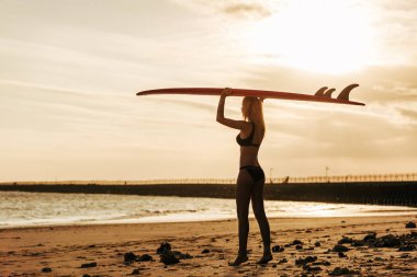 kadın sörfçü gün batımında başına surfboard ile poz