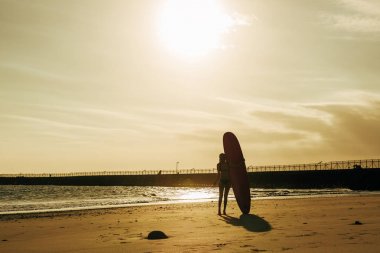 arkadan görünüşü sörfçü gün batımında sahilde surfboard ile poz