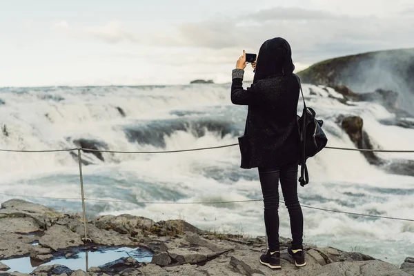 Vista posteriore di giovane donna che fotografa maestosa cascata in Islanda — Foto stock