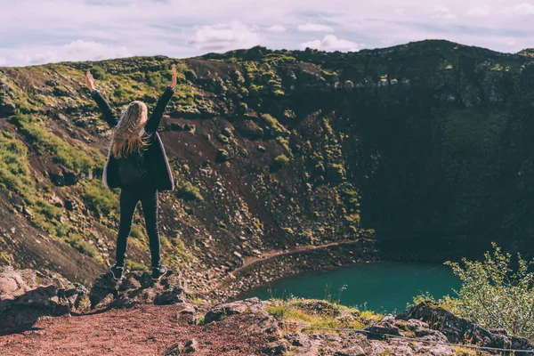 Vista trasera de la chica de pie con las manos levantadas y mirando el hermoso lago del cráter en Islandia - foto de stock