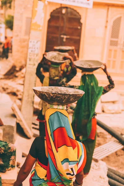 Vue arrière des femmes en vêtements traditionnels lumineux portant des bols sur les têtes, rajastan, jeisalmir — Photo de stock