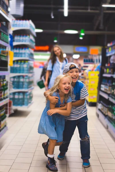Soeur heureuse et frère s'amuser au supermarché, mère debout derrière — Photo de stock