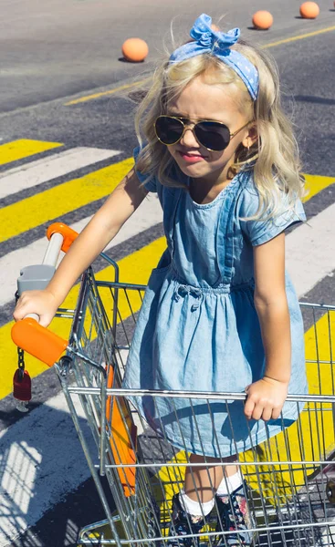 Pequena criança adorável em óculos de sol se divertindo no carrinho de compras na passarela — Fotografia de Stock