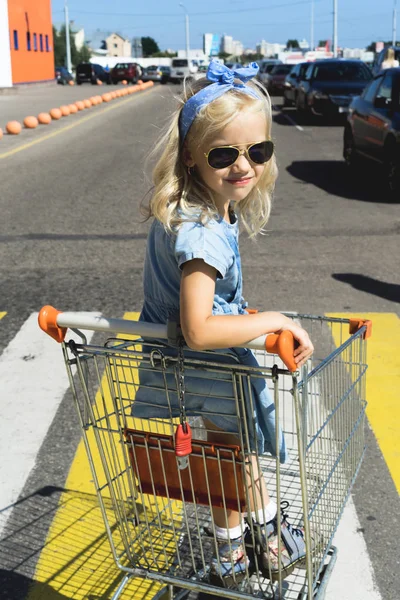 Little adorable female child having fun in shopping cart at parking — Stock Photo