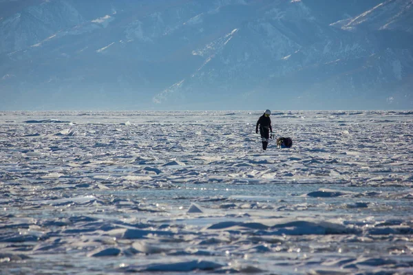 Caminhante masculino com mochila andando na superfície da água gelada contra picos na costa, Rússia, lago baikal — Fotografia de Stock