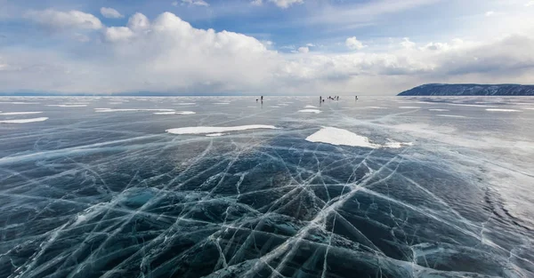 View of ice water surface under cloudy sky during daytime and group of hikers on background , russia, lake baikal — Stock Photo